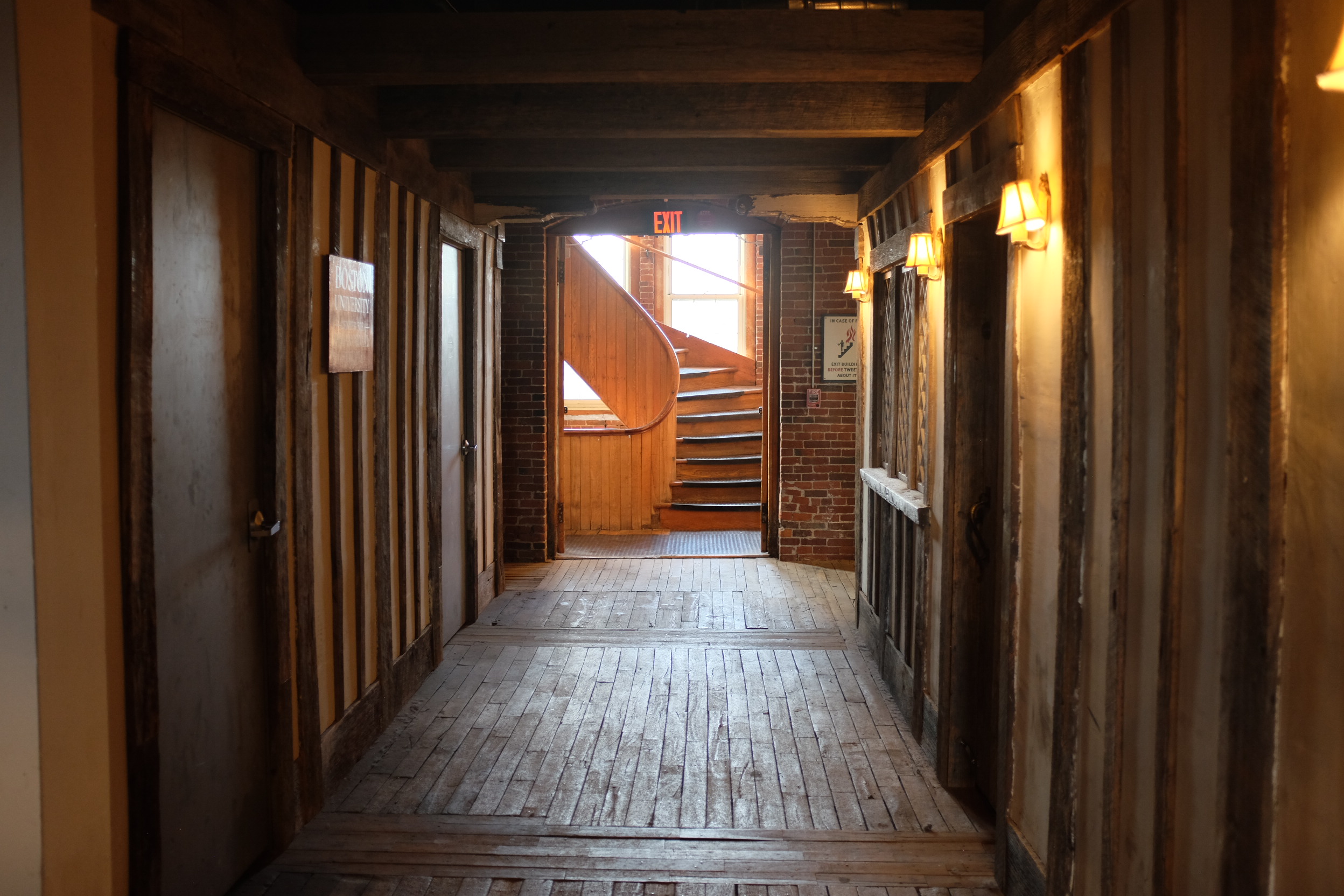 A photo of an old wooden hallway with a spiral staircase curving upwards visible through a door at the end.