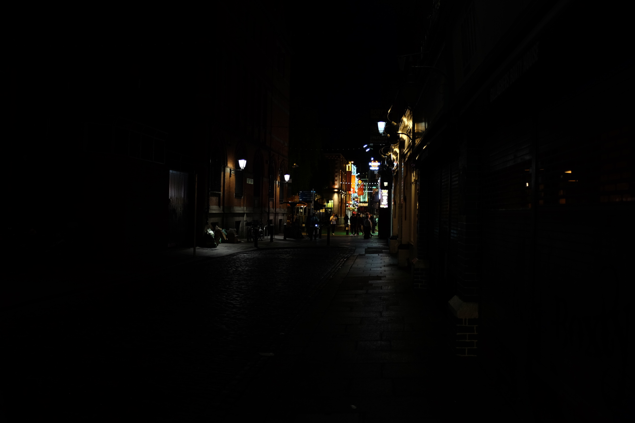 A photo of a dark city street with bright lights in the distance.